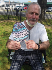 senior man sitting in chair taking photo with a paper easter egg fan