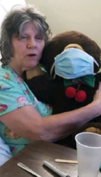 resident sitting with her teddy bear who is wearing a medical mask