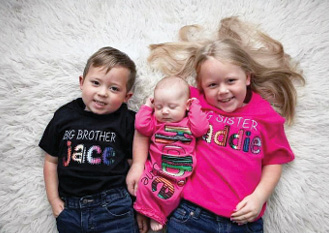 Young girl young boy and newborn girl laying on white carpet looking up for a photograph