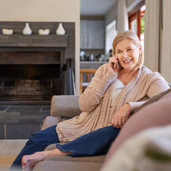 Adult woman sitting on sofa at home talking on the telephone