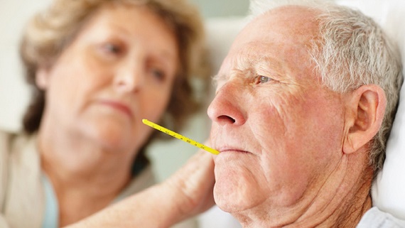 older adult man with thermometer in mouth being comforted by wife