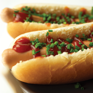 photo of two plated hot dogs with ketchup and chives