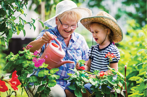 grandmother gardening with granddaughter, watering flowers on sunny day