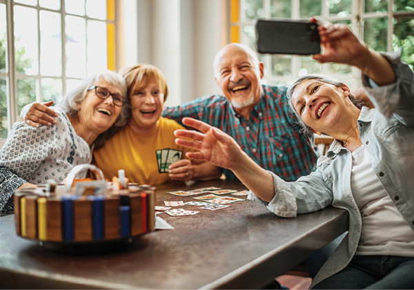 Group of older adults, men and women, taking a selfie while playing card games at home